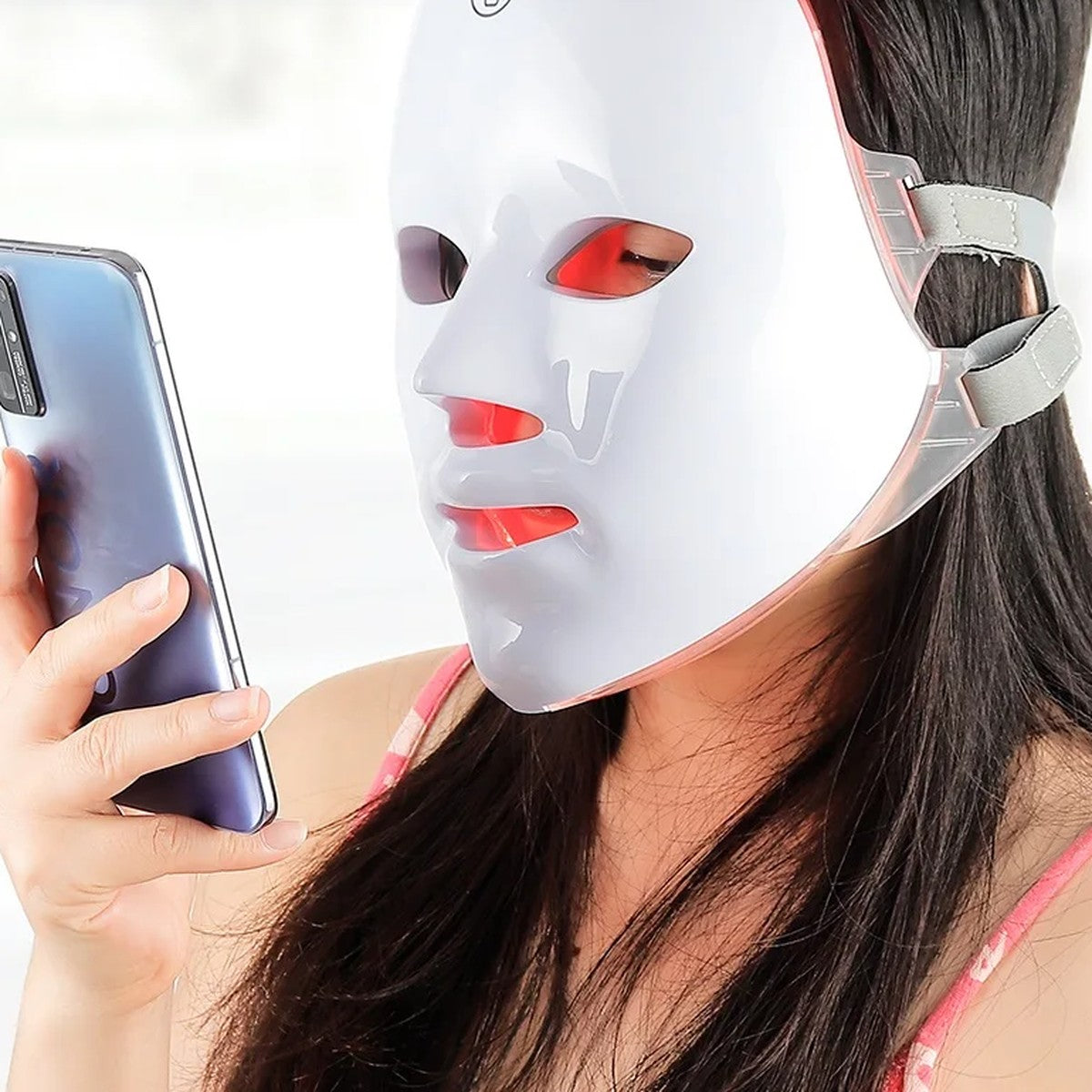 Žena s nasazenou LED maskou si čte na telefonu